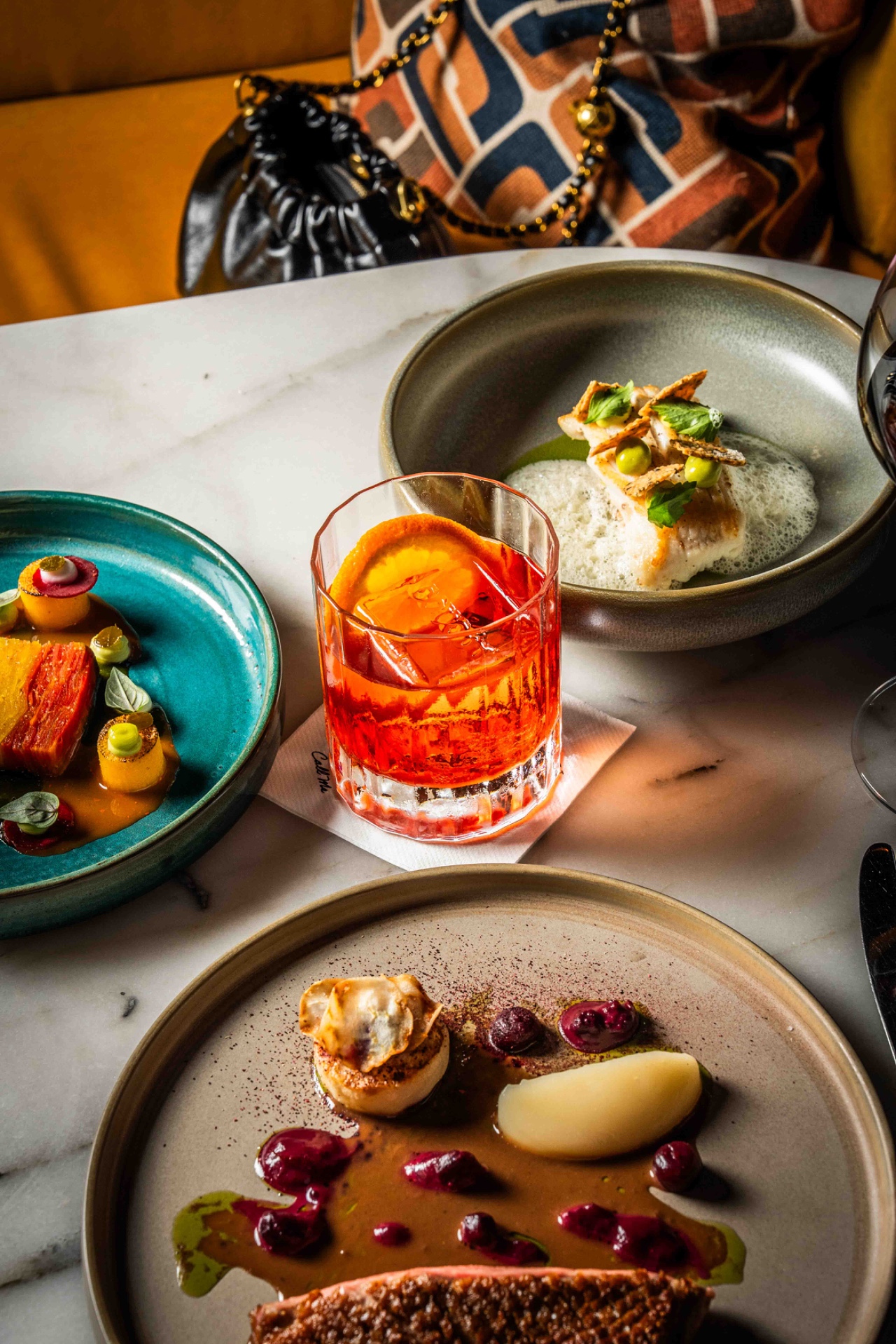 Drie fijne gerechten en een negroni op een marmeren tafel