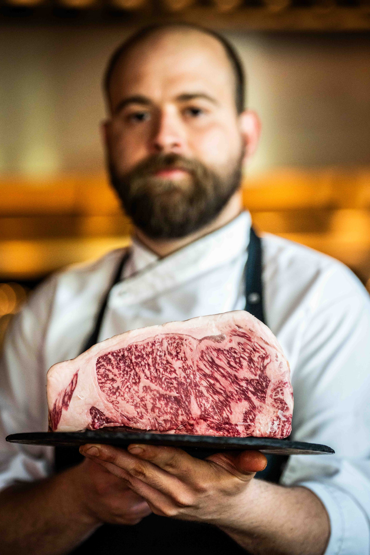 Chef presenteert een royaal gemarmerde wagyu-rib op een leisteen plank
