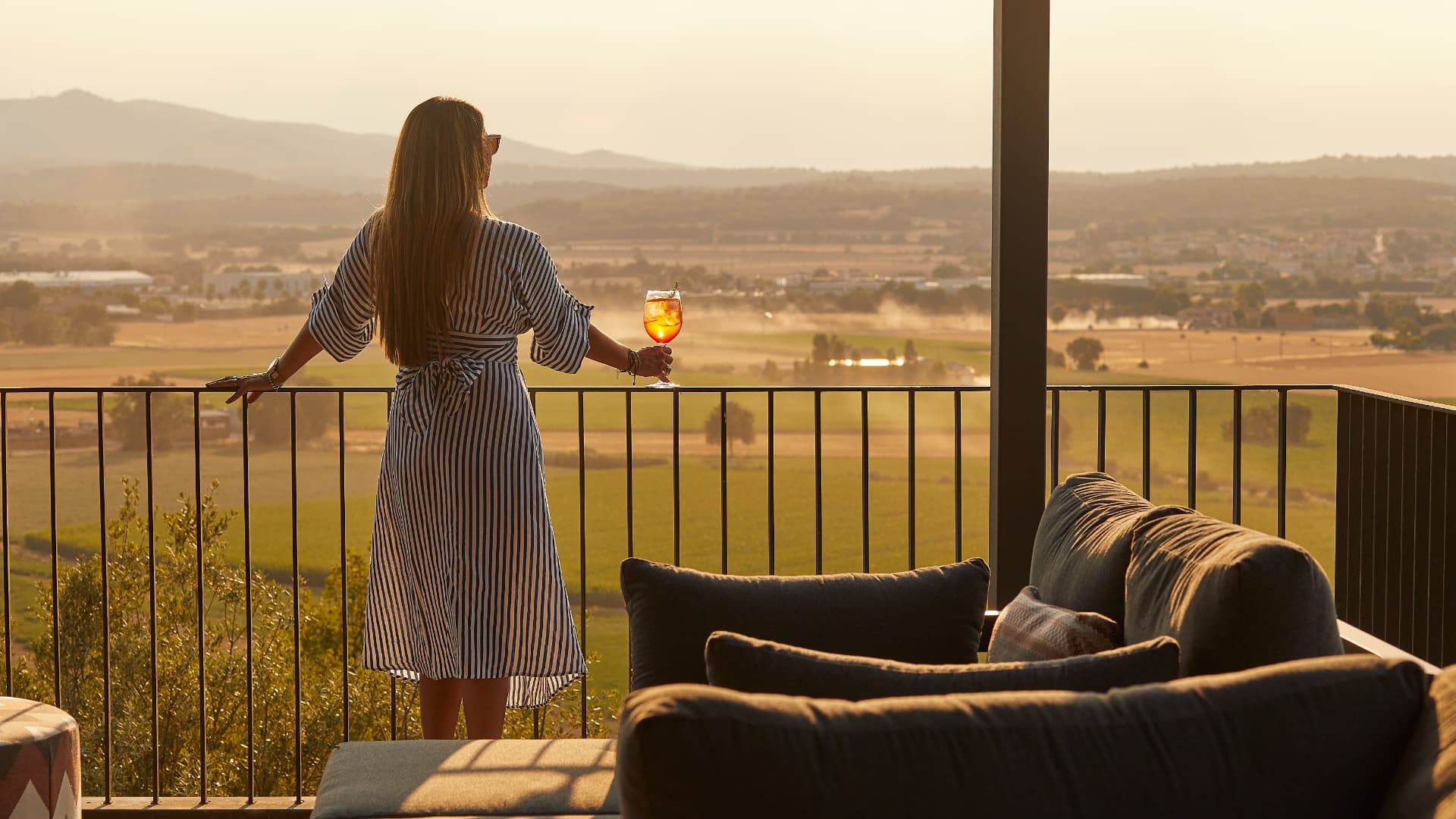 Vrouw met een spritz op een terras met uitzicht over heuvels bij zonsondergang