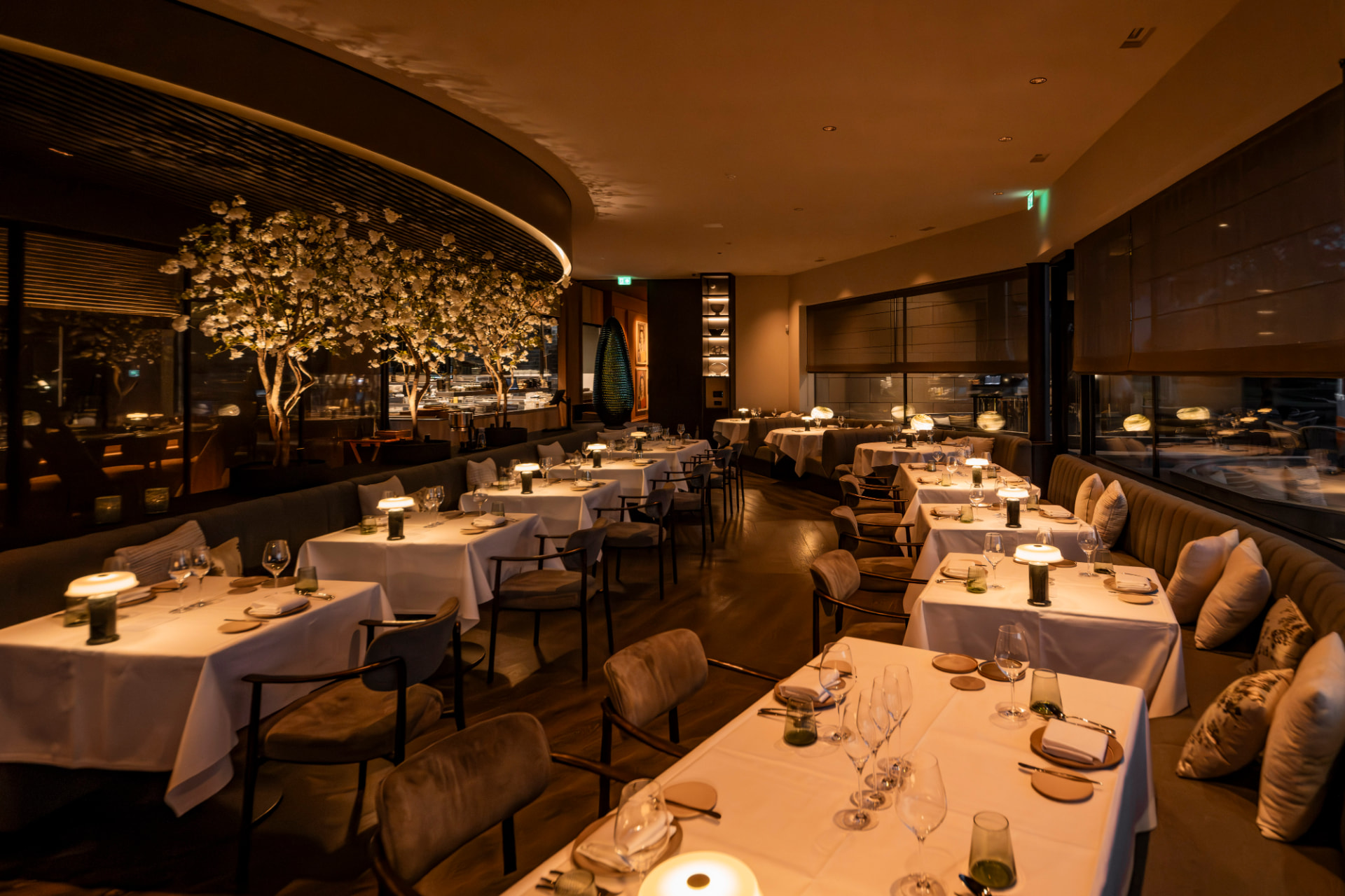 Warm verlicht restaurantinterieur met witte tafellinnen en bloesembomen